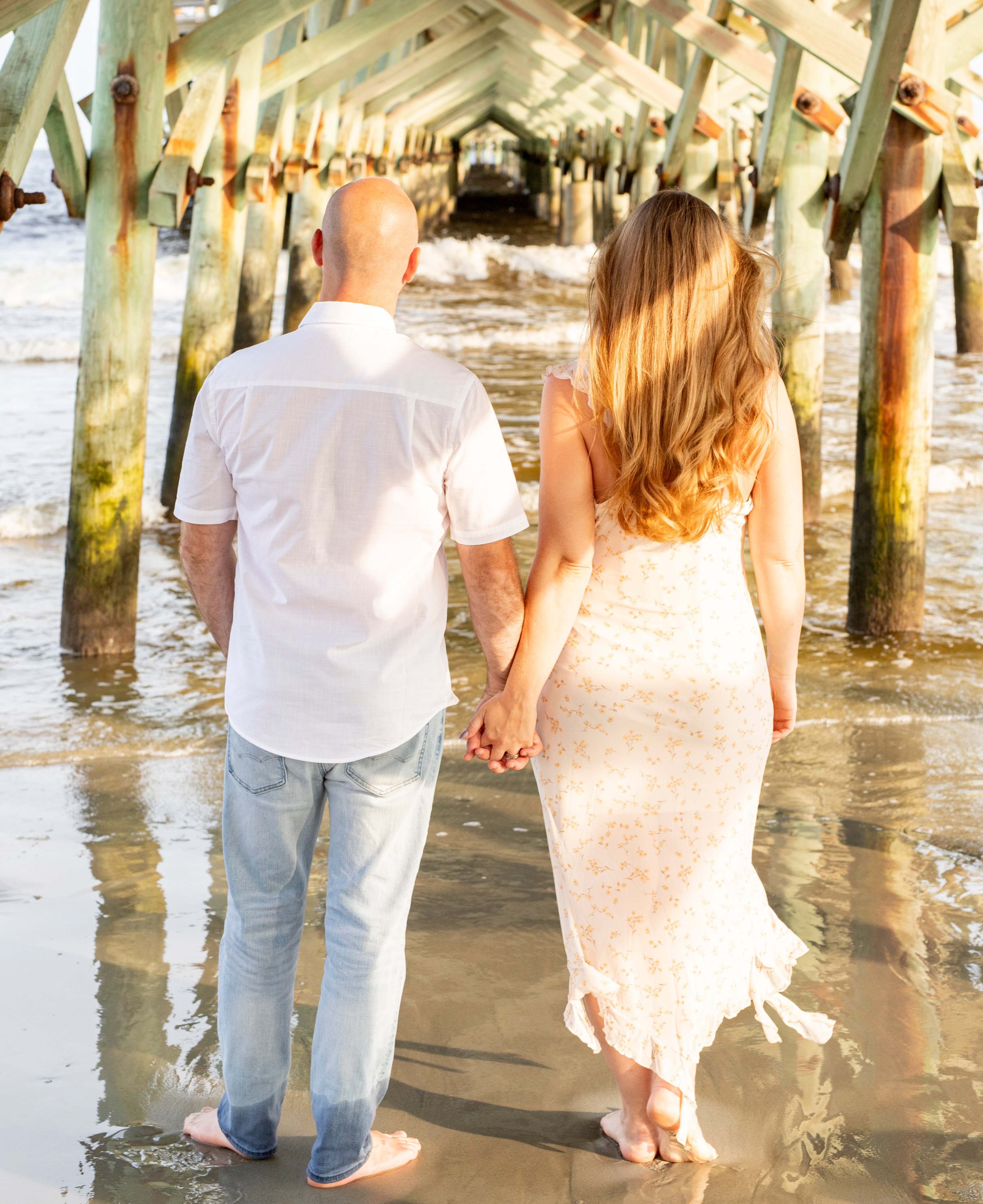 Man and woman at the beach with backs to camera holding hands