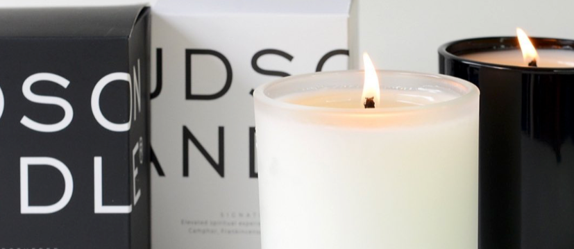 black and white lit candles burning in front of Hudson Candle labelled boxes